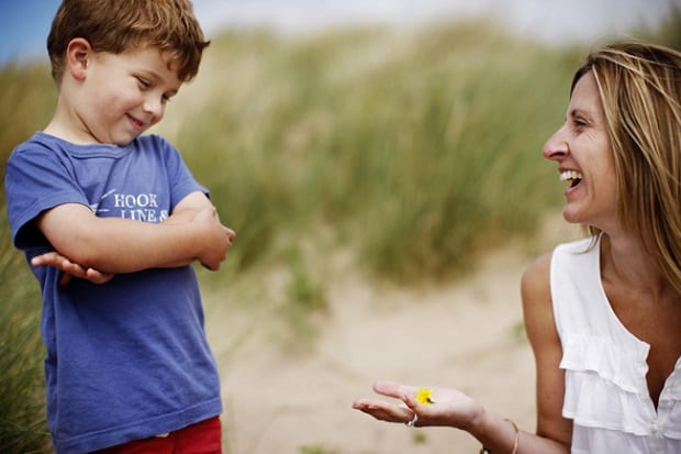 A boy grinning at the flower his mother is holding