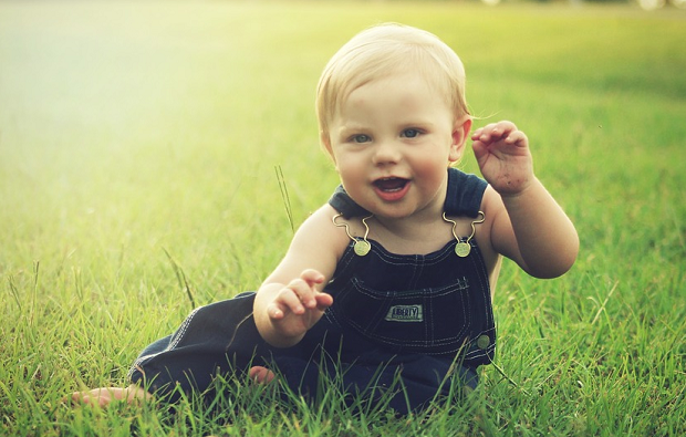 A picture of a baby sitting on the grass on a bright sunny day