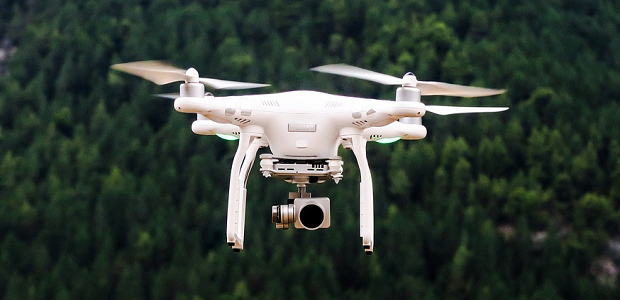 A camera equipped drone flying over a deep green forest