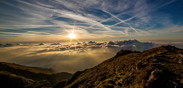 A scenic mountain view, with the sun shining brightly over some clouds