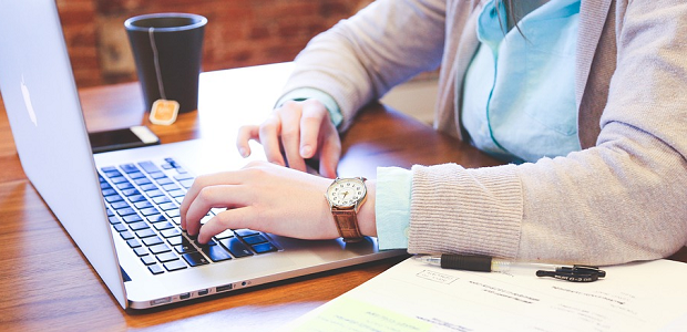 A person in a grey jacket working on a laptop at their desk