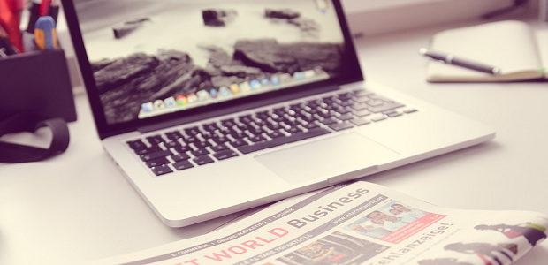 A toned-down image of a newspaper sitting on a table in front of an open laptop