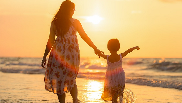 A mom and her daughter taking a stroll on the beach in front of the sunset