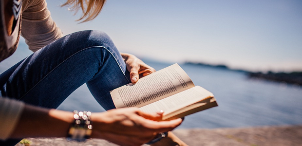 A woman sitting by the ocean reading a book