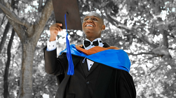 A graduating student holding up his graduation cap