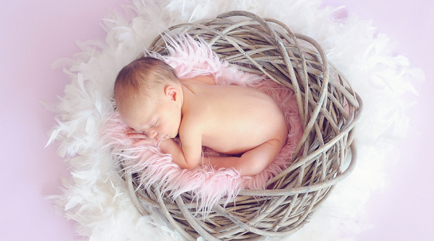 An overhead shot of a very young baby laying in a basket