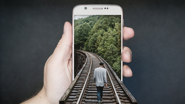 An image of a man walking on a railroad, which extends out of the phone the image is displayed on