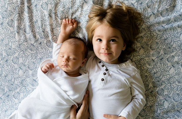 A baby laying on a blanket with their big sister