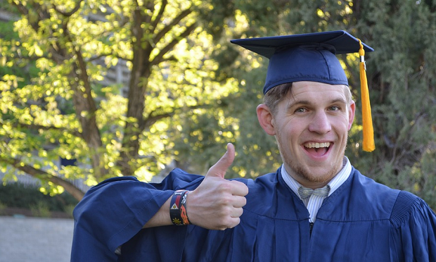 A man in a blue graduation gown giving a thumbs up