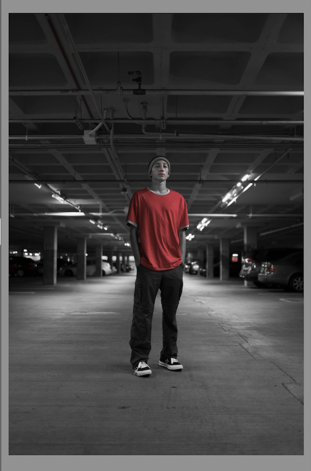 Original image appears black and white, except for red tones in the man's shirt, face, and in the taillights of some cars in the background.