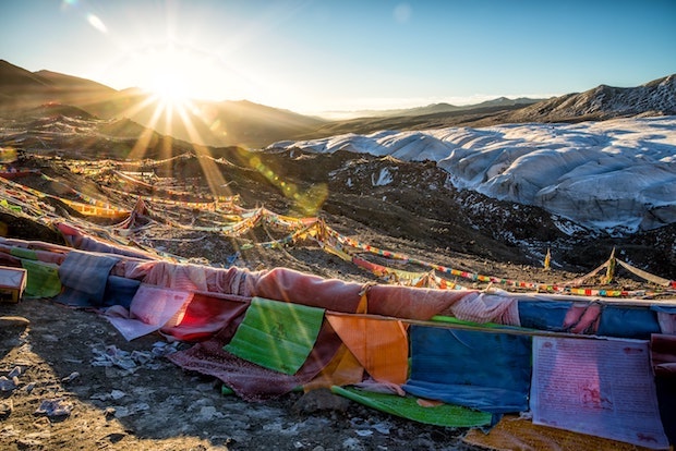 Sun glaring over mountains with colorful fabric strung in the foreground