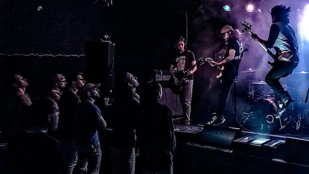 3 musicians playing guitar on stage while small crowd watches