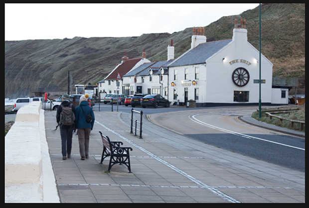 Seaside pub named "The Ship" on the right with travelers walking toward it on the left