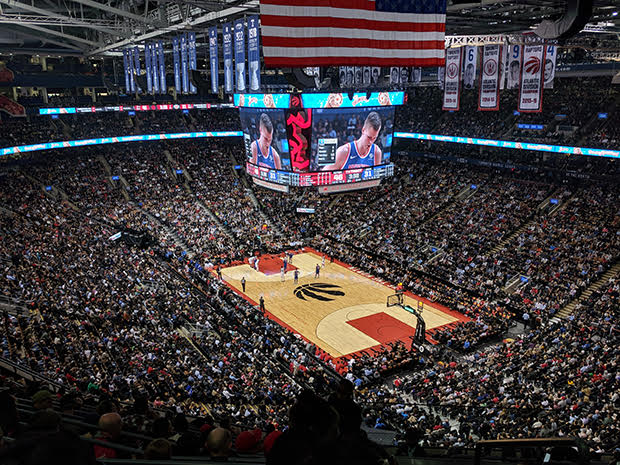 Crowded basketball sports arena featuring basketball court, jumbotron coverage, and fans in seats