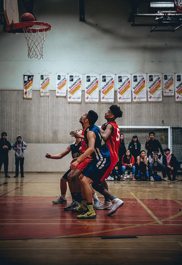 4 basketball players on a court, 2 from each team, look up at the ball going into the net