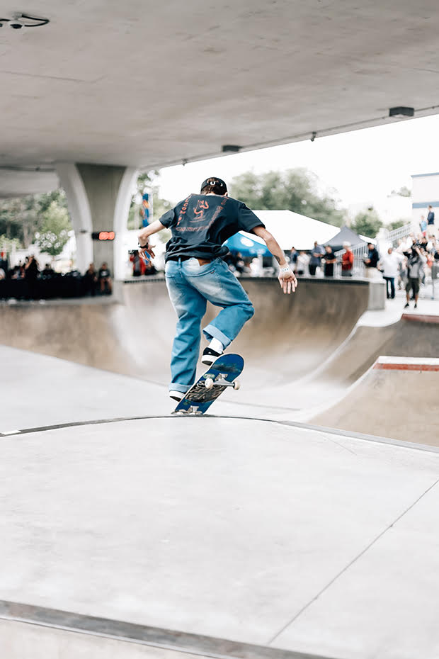 Skateboarder with his back to the camera in the middle of a trick in which the back wheels of his board are off the ground.