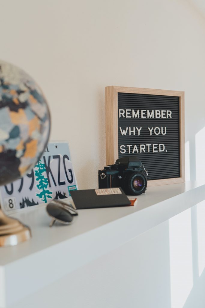 A globe, a camera, a sunglasses, and a wall art placed on a white colored table top