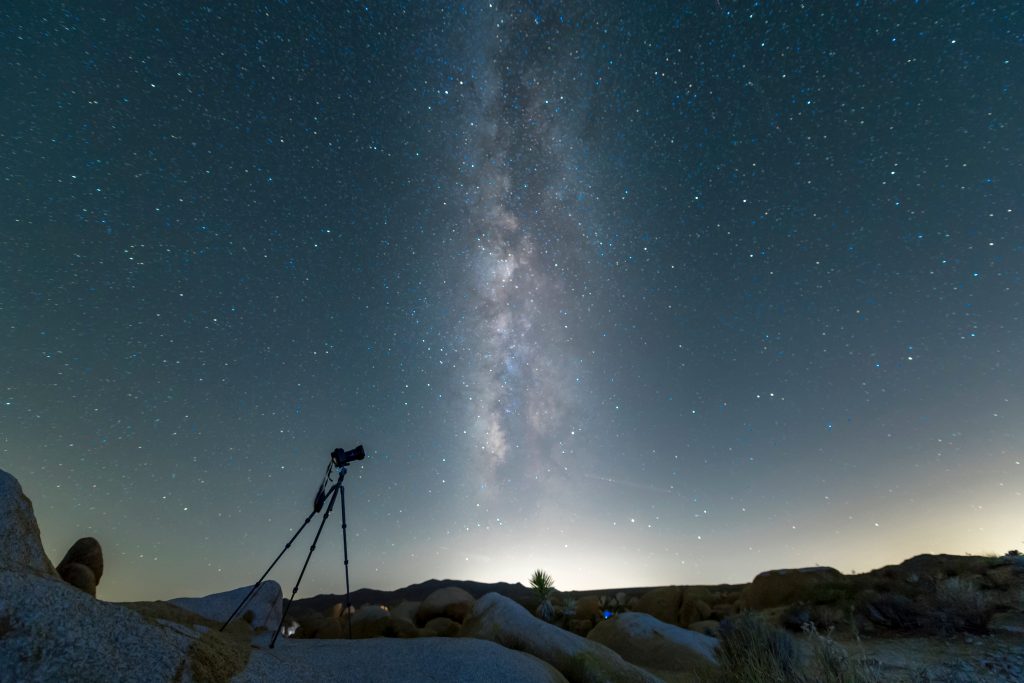 A camera mounted on a tripod stand placed on a rock with the Milky Way at the background