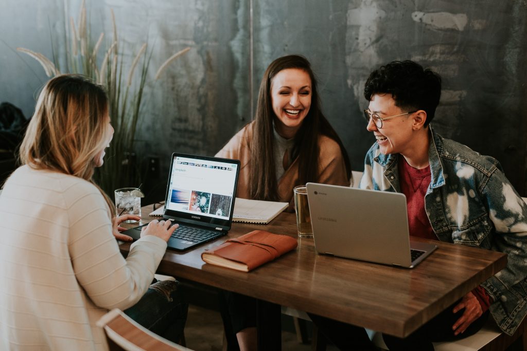 Three people sitting across the table talking and working on their laptops