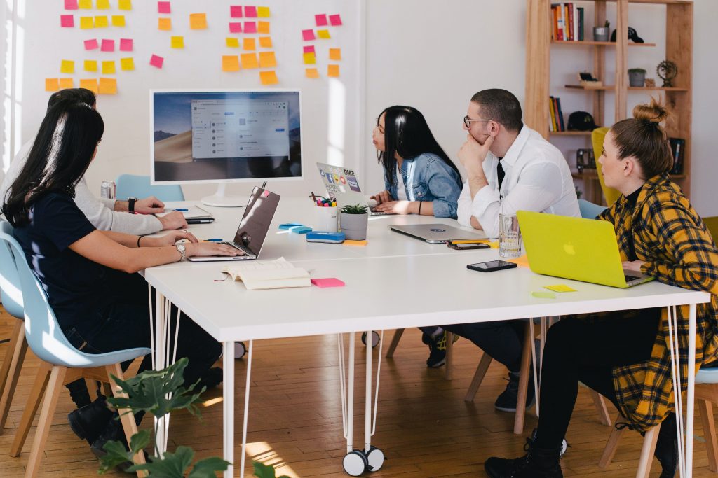 Five people sitting across the table discussing something while looking at the monitor