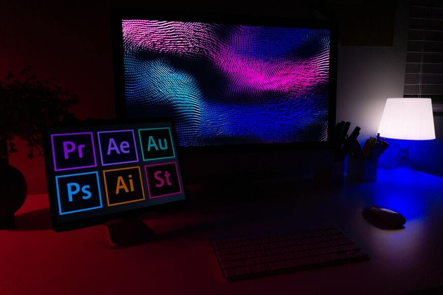 Two PCs, one displaying a wallpaper, the other different logos of Adobe applications