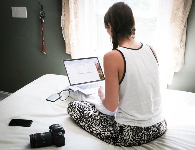 A women sitting on the bed while working on a laptop