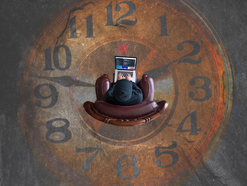 Brown analog clock photo with a man sitting in the center with his laptop