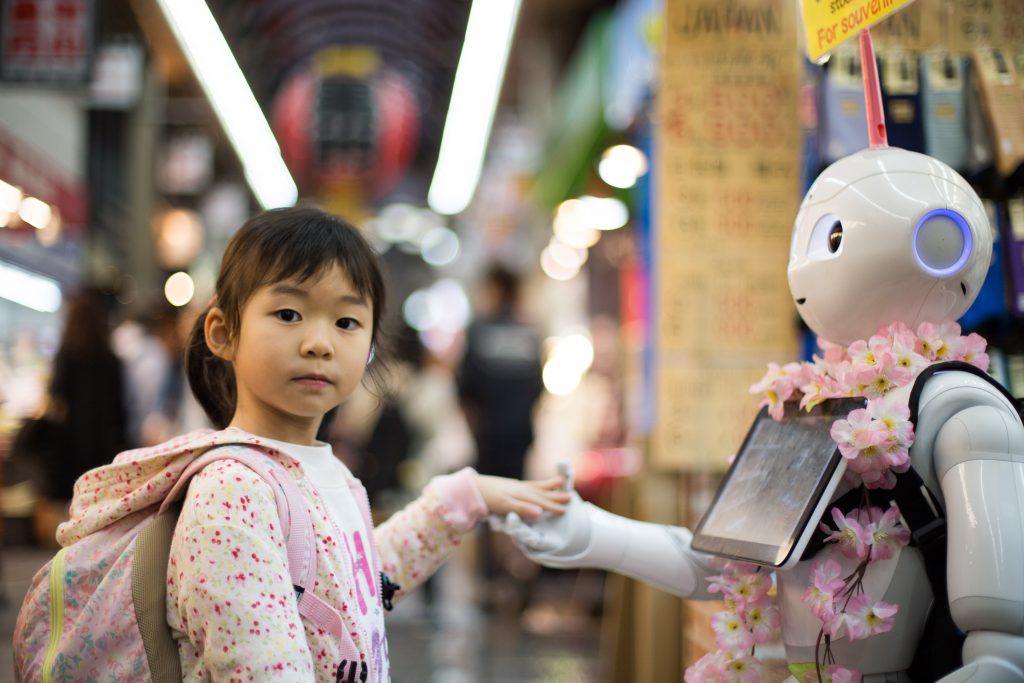 A kid shaking hands with a robot equipped with a tablet with facial recognition feature on it