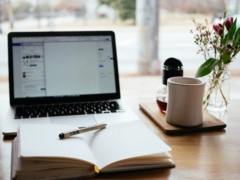 A laptop with an open book and coffee kept on the table