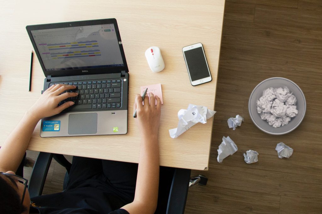 A high angle shot of a person working on a laptop and scribbling notes