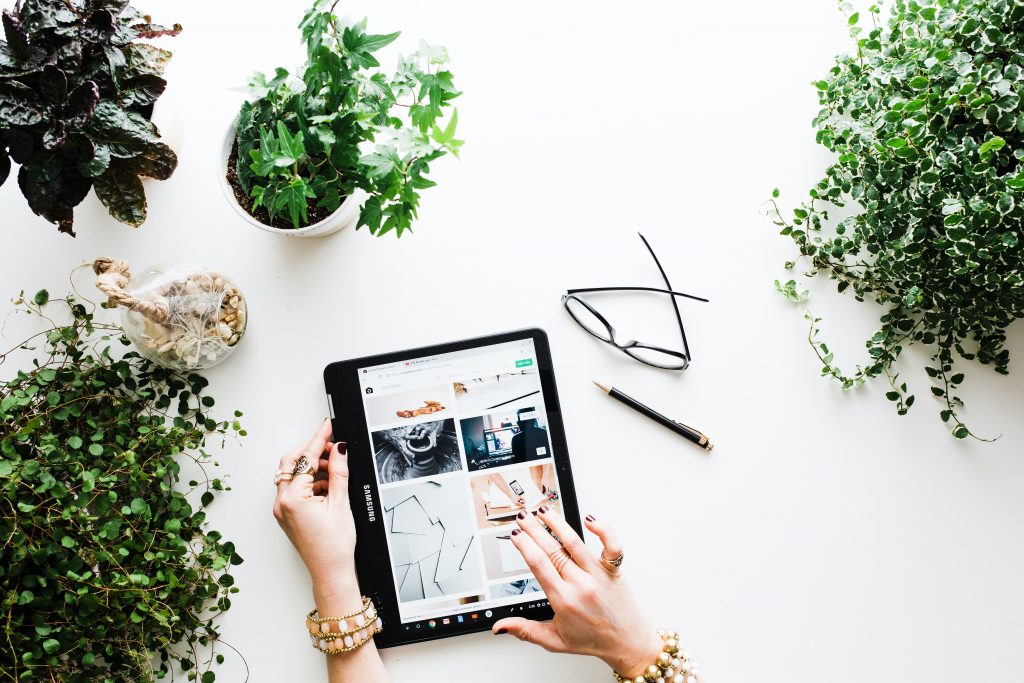 A high-angle shot of a table top with some plants and a tablet displaying a photo gallery